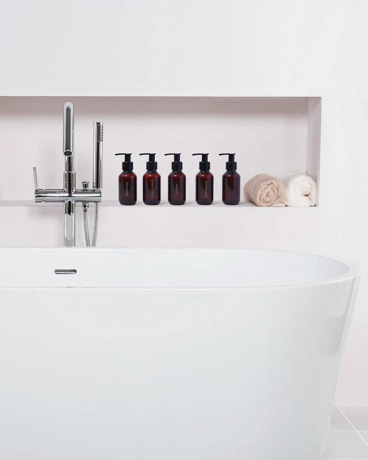 Bathroom setting with a white bathtub, faucet, and amber bottles on a shelf