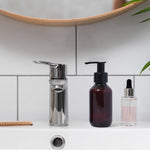 Bathroom sink with soap dispenser, amber bottle, and clear dropper bottle against a tiled wall