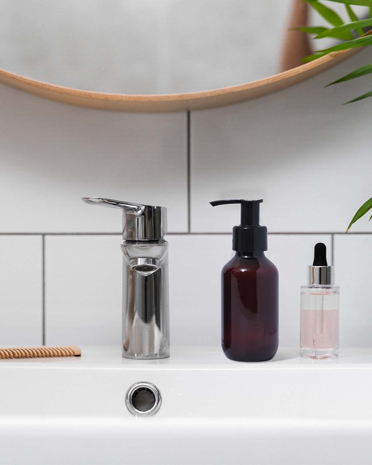 Bathroom sink with soap dispenser, amber bottle, and clear dropper bottle against a tiled wall