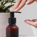 Hand using a pump bottle with a plant in the background