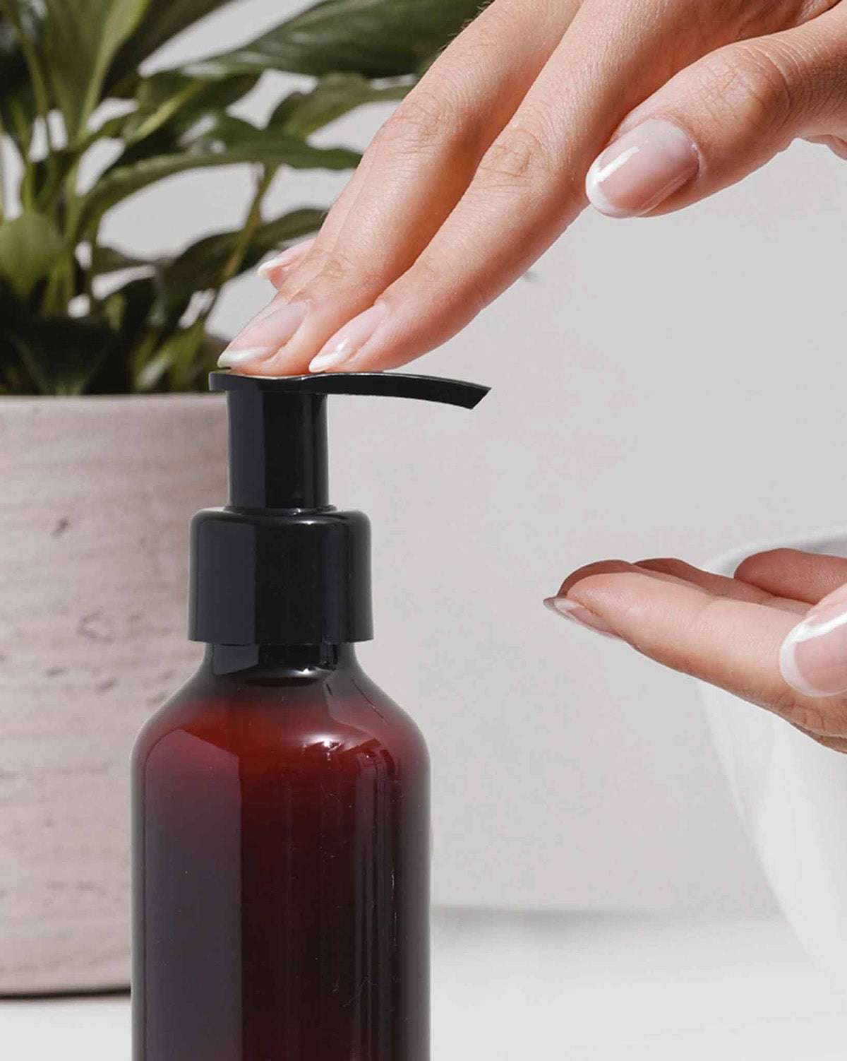 Hand using a pump bottle with a plant in the background