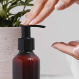 Hand using a pump bottle with a plant in the background