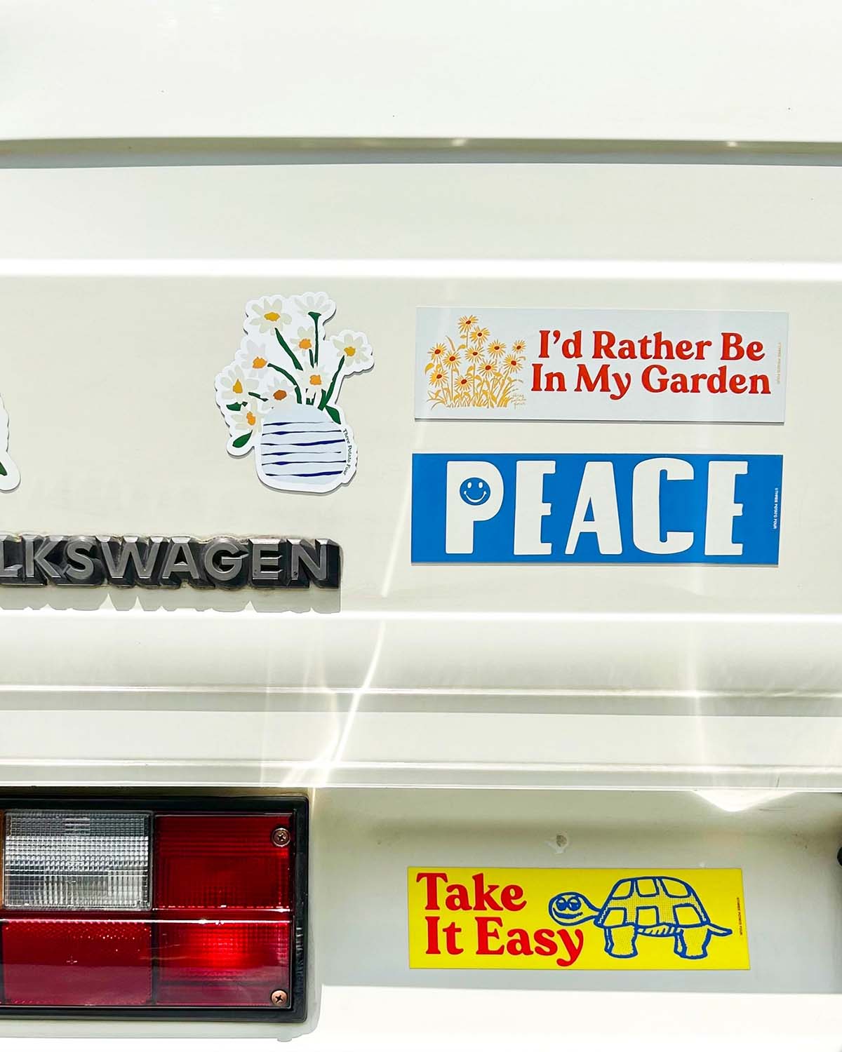 Decorative stickers on a Volkswagen vehicle, including 'I'd Rather Be In My Garden', 'PEACE', and 'Take It Easy'