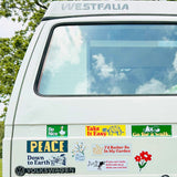 White van with various stickers on the back window, including a Volkswagen logo, with trees and sky in the background