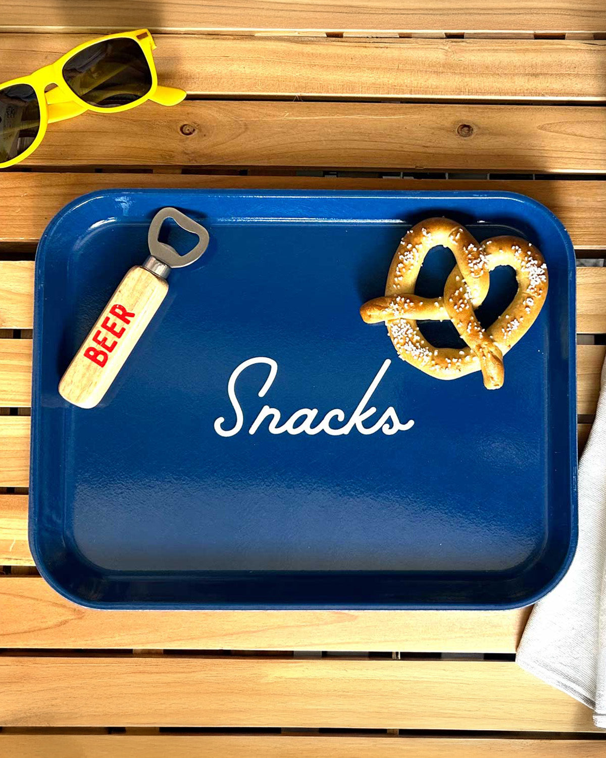 Blue tray with 'Snacks' text, bottle opener, and pretzel on a wooden surface