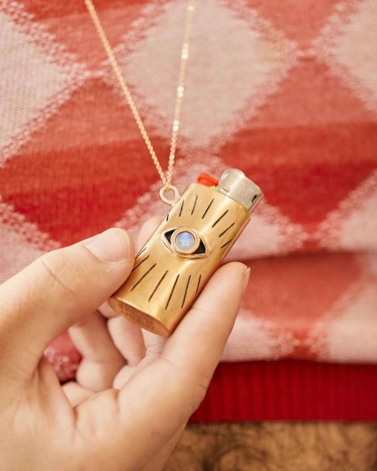 Gold lighter with blue gemstone held by a hand against a red plaid background