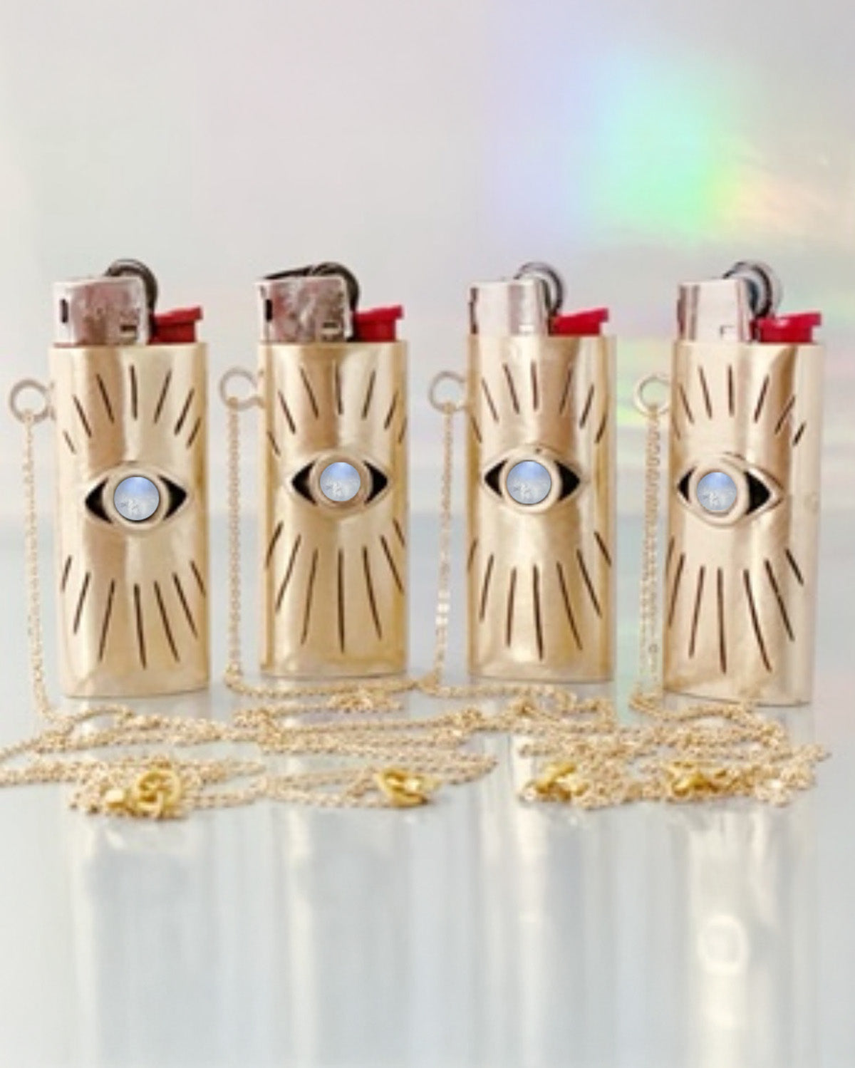 Four gold lighters with eye designs on a white background