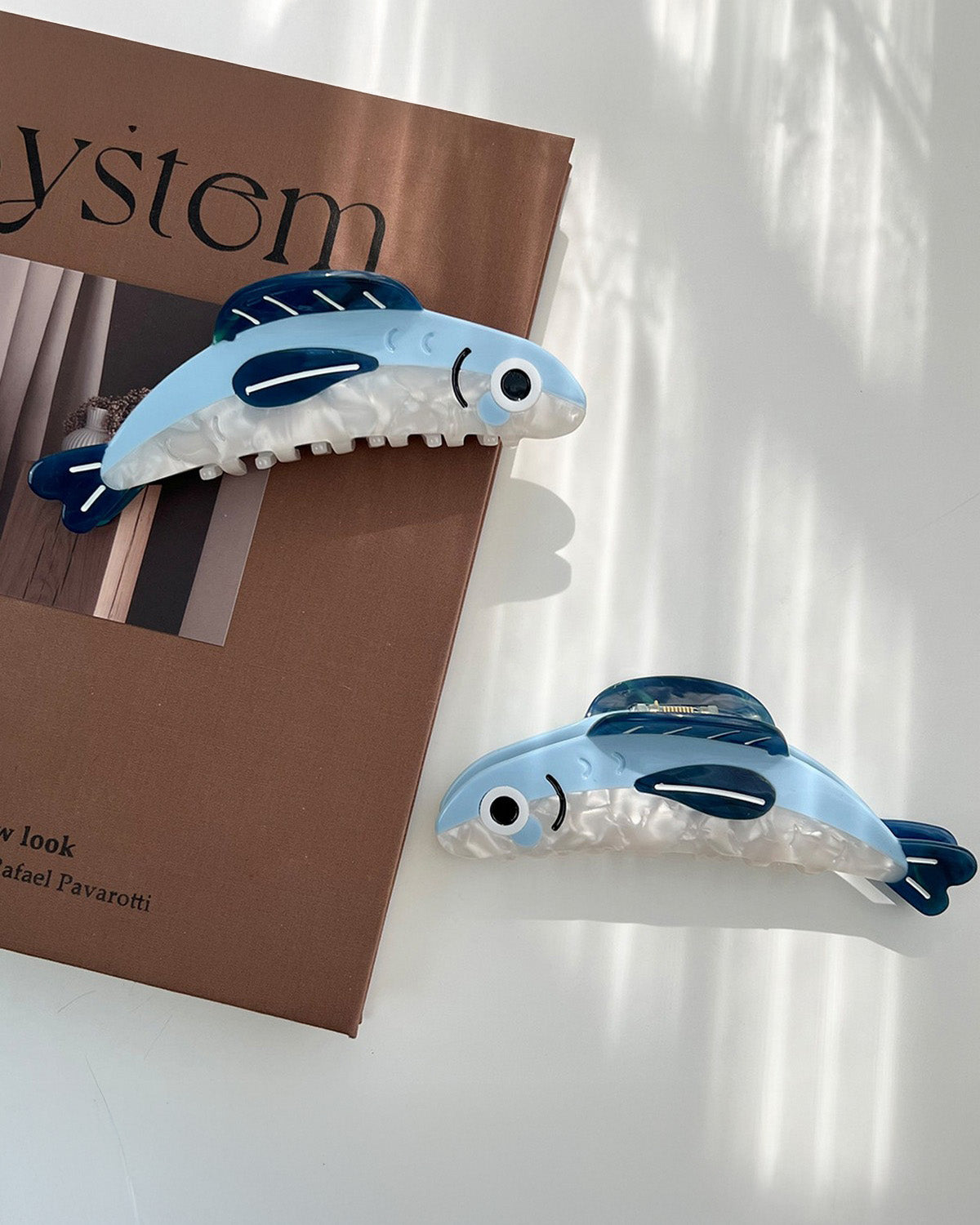 Blue and white shark-shaped hair clips on a white surface with a brown box in the background