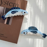 Blue and white shark-shaped hair clips on a white surface with a brown box in the background