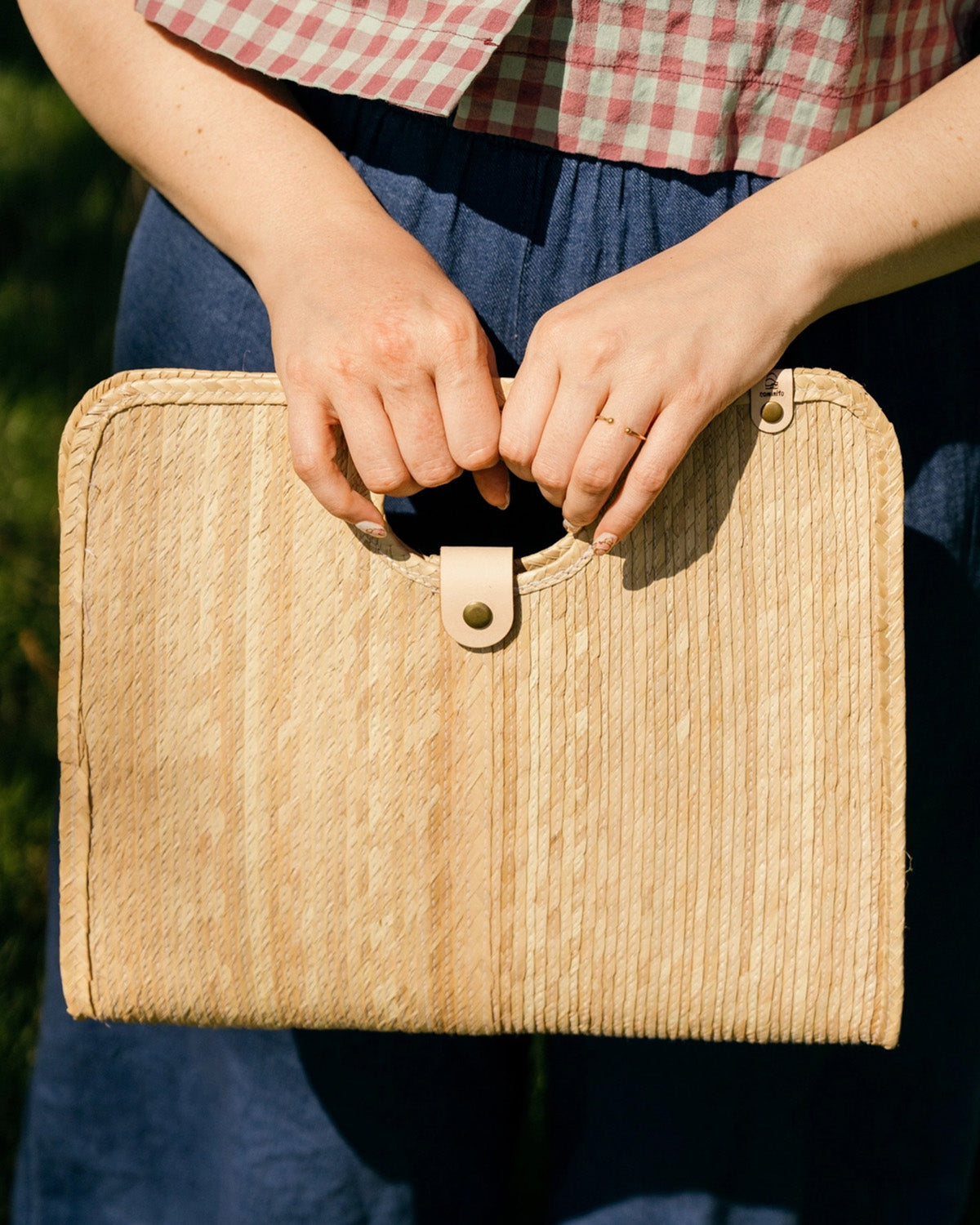 Model holding palm fiber woven tan bag on a white background