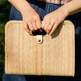 Model holding palm fiber woven tan bag on a white background