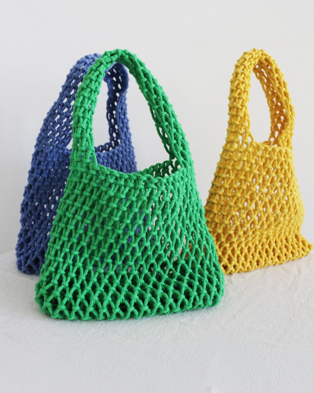 Three colorful mesh bags in green, blue, and yellow on a light background