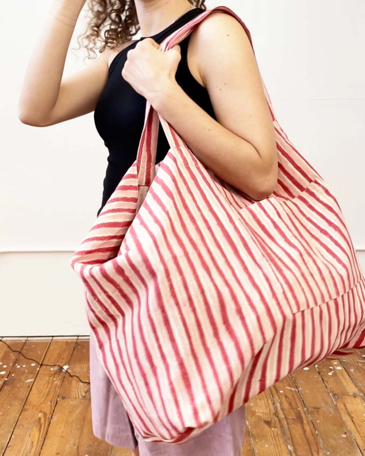 Person holding a red and white striped bag on a wooden floor