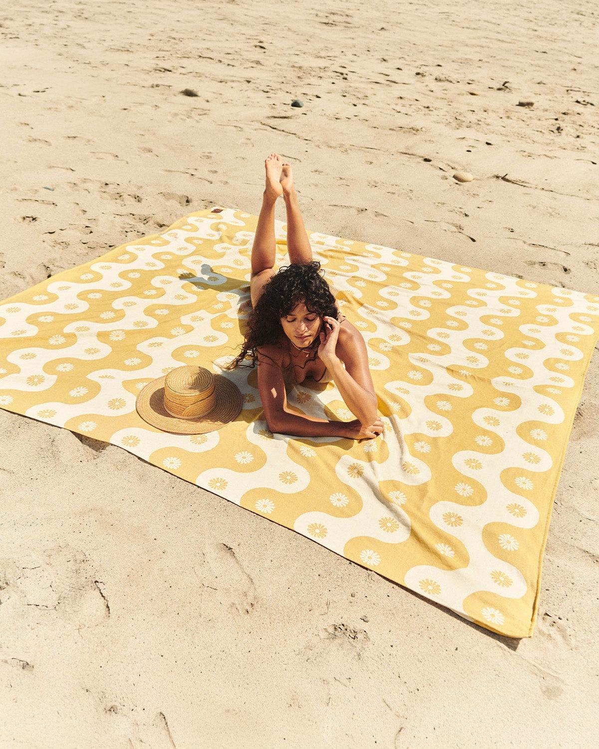Woman lying on a yellow and white patterned beach towel on sand