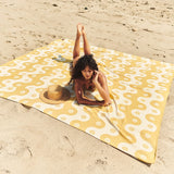Woman lying on a yellow and white patterned beach towel on sand