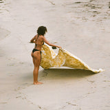 Woman holding a yellow patterned towel on a sandy beach