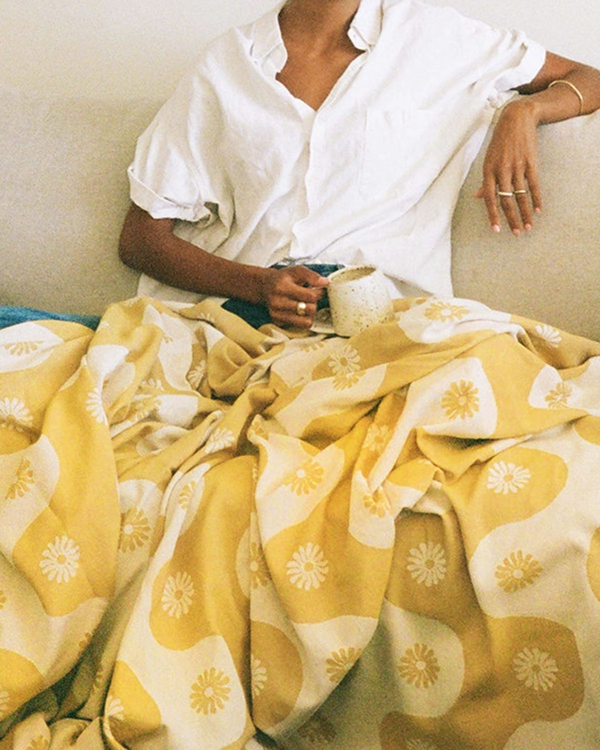 Person wearing a white shirt sitting on a couch with a yellow patterned blanket