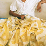 Person wearing a white shirt sitting on a couch with a yellow patterned blanket