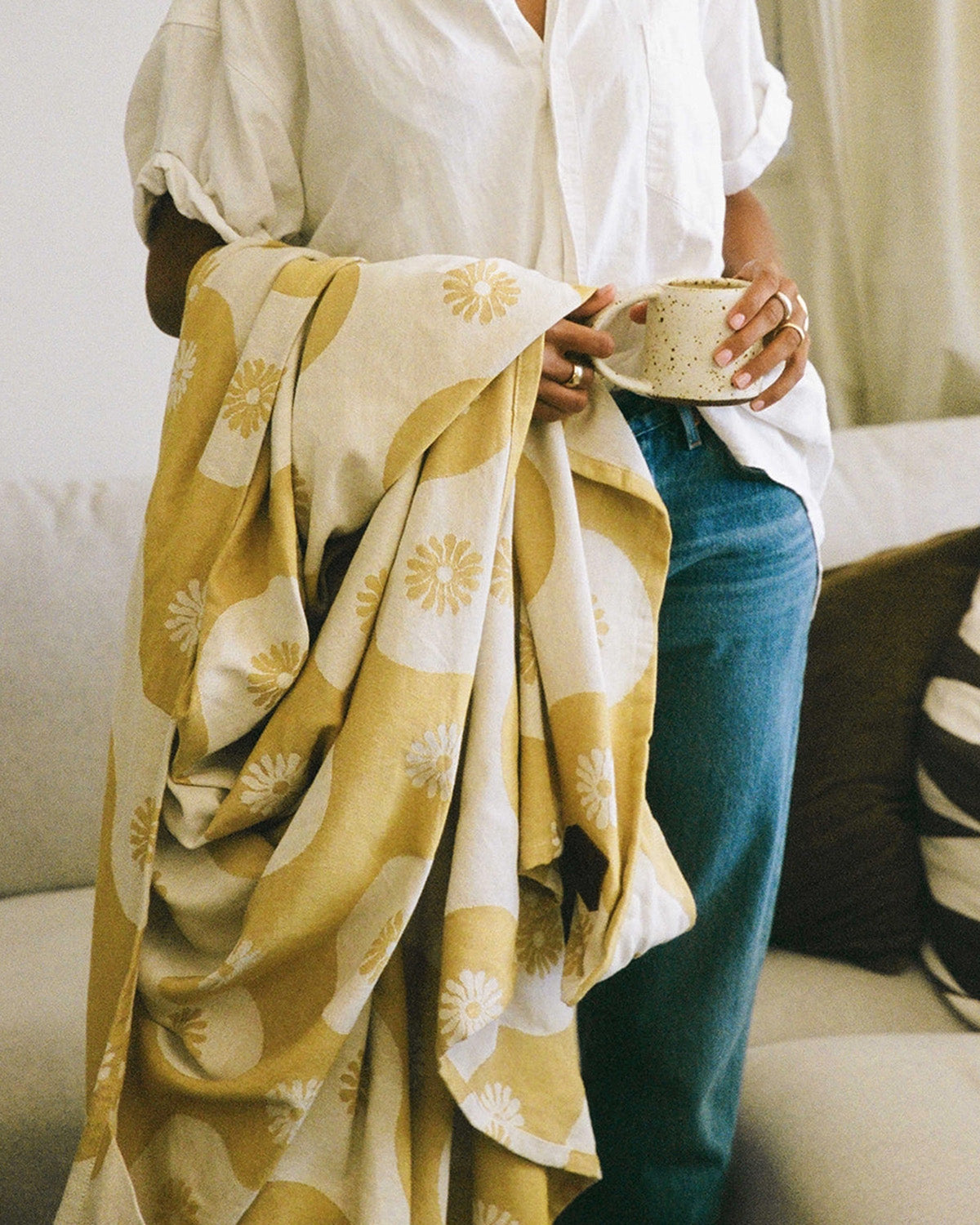 Person holding a cup wrapped in a yellow and white patterned blanket on a couch