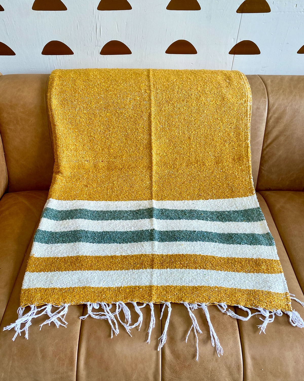 Yellow blanket with green and white stripes draped over a brown couch against a light blue wall with brown circular decorations