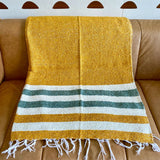 Yellow blanket with green and white stripes draped over a brown couch against a light blue wall with brown circular decorations