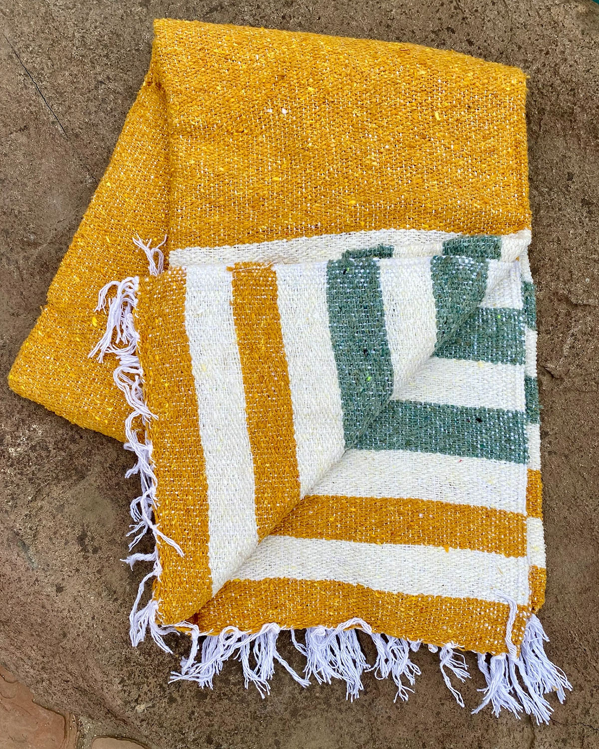 Yellow and green striped towel with white fringe on a stone surface