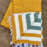 Yellow and green striped towel with white fringe on a stone surface