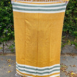 Yellow towel with green and white stripes on a paved surface with greenery in the background