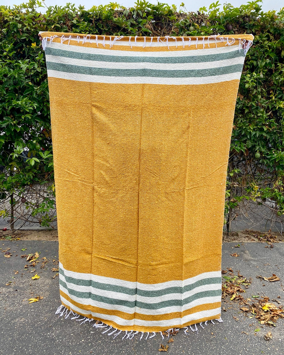 Yellow towel with green and white stripes on a paved surface with greenery in the background