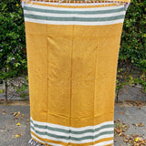 Yellow towel with green and white stripes on a paved surface with greenery in the background
