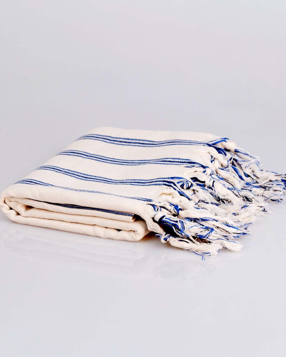 Folded towel with blue stripes and tassels on a light gray background