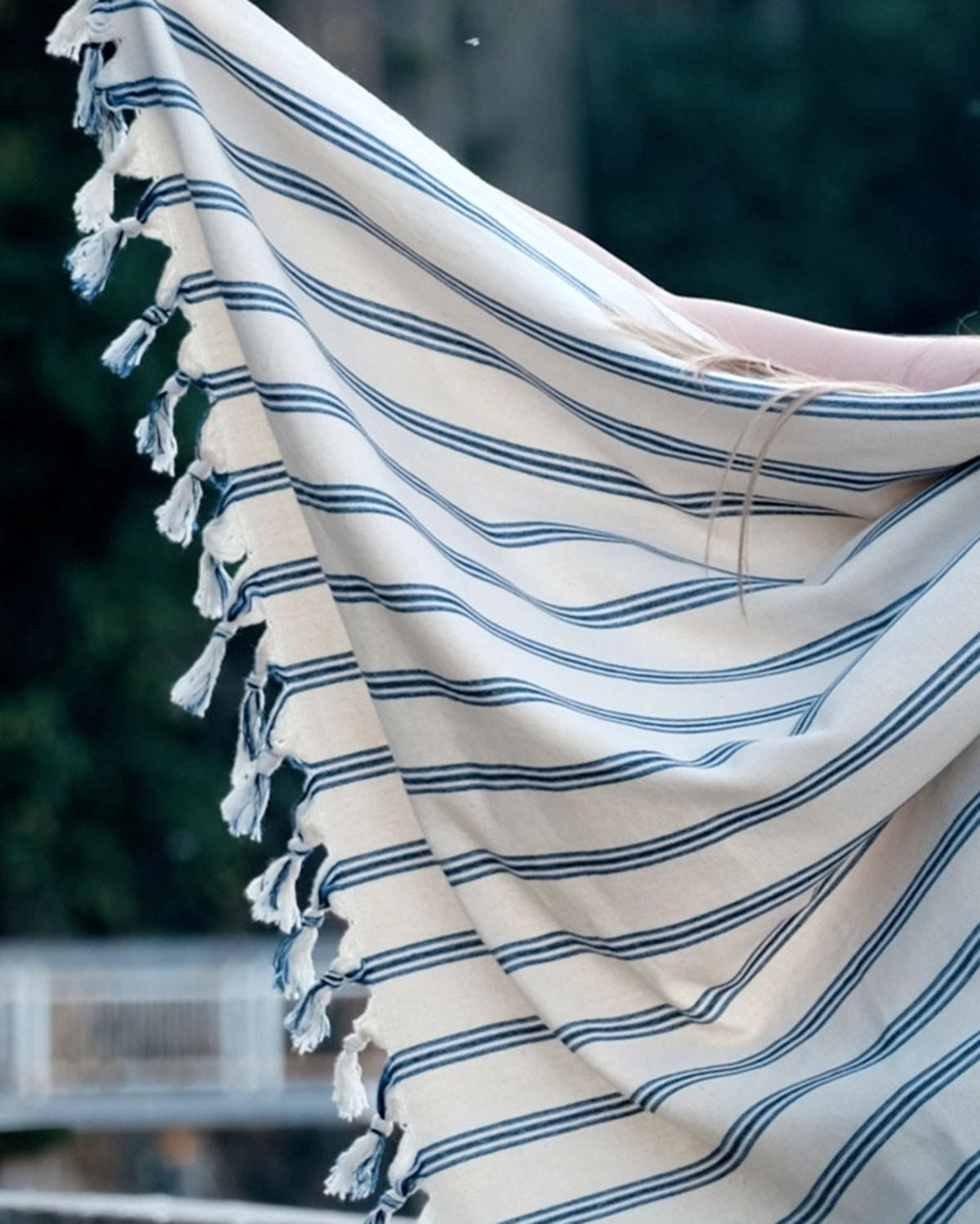 Beige towel with blue stripes and tassels draped over a chair outdoors