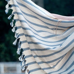 Beige towel with blue stripes and tassels draped over a chair outdoors
