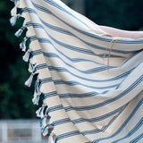 Beige towel with blue stripes and tassels draped over a chair outdoors