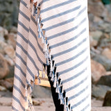 Striped towel with tassels held by a person on a rocky beach