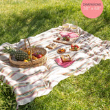 Striped picnic blanket with food on a grassy field, dimensions displayed.