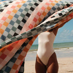 Person in a swimsuit holding a colorful checkered towel on a beach