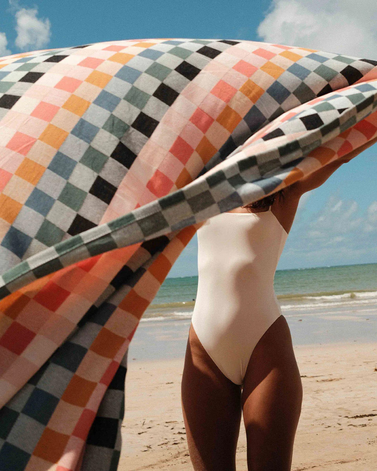 Person in a swimsuit holding a colorful checkered towel on a beach