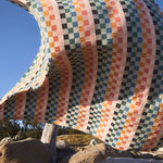 Colorful checkered blanket draped over a large rock with a clear blue sky in the background.