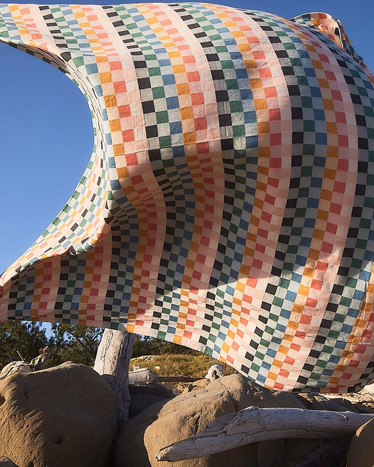 Colorful checkered blanket draped over a large rock with a clear blue sky in the background.