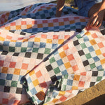 Person sitting on a colorful checkered blanket by the beach
