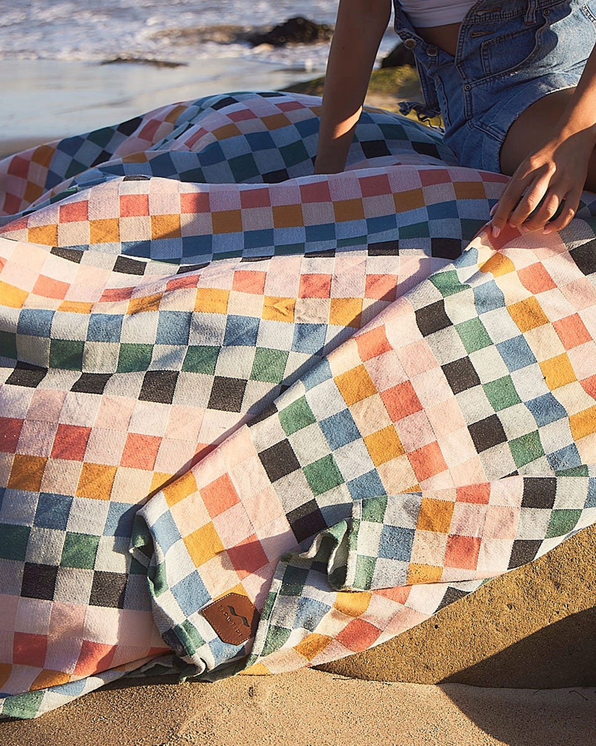 Person sitting on a colorful checkered blanket by the beach