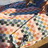 Person sitting on a colorful checkered blanket by the beach