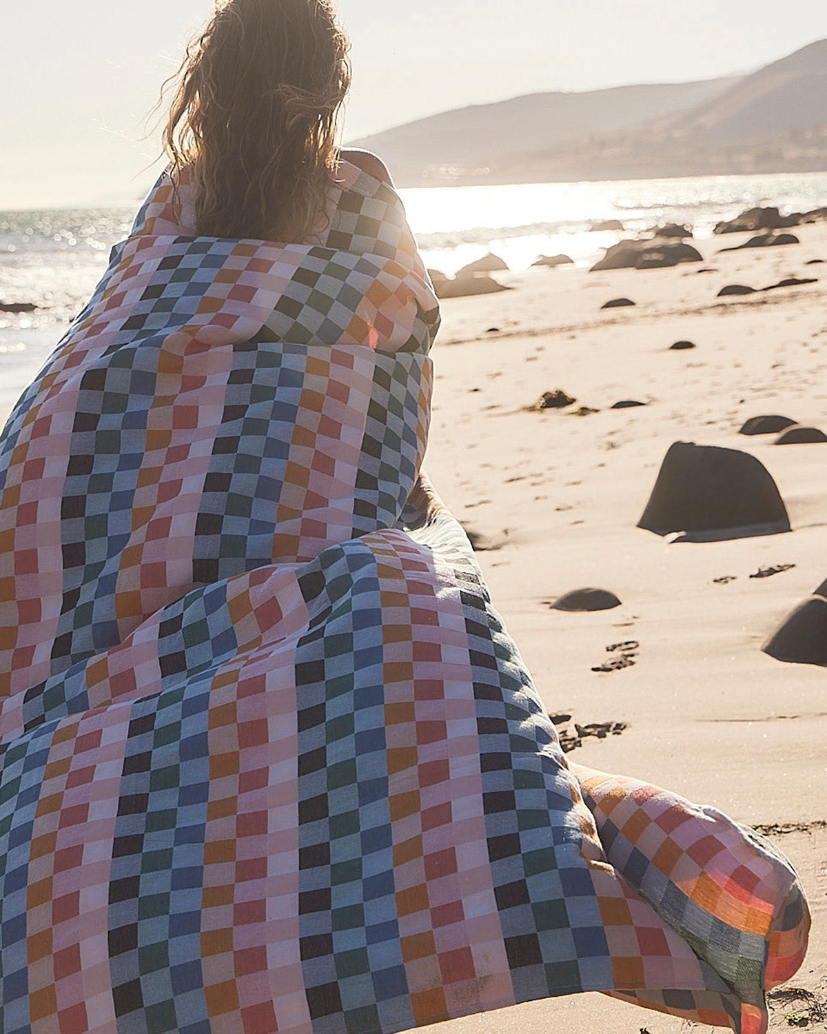 Person wrapped in a colorful checkered blanket on a beach