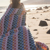 Person wrapped in a colorful checkered blanket on a beach