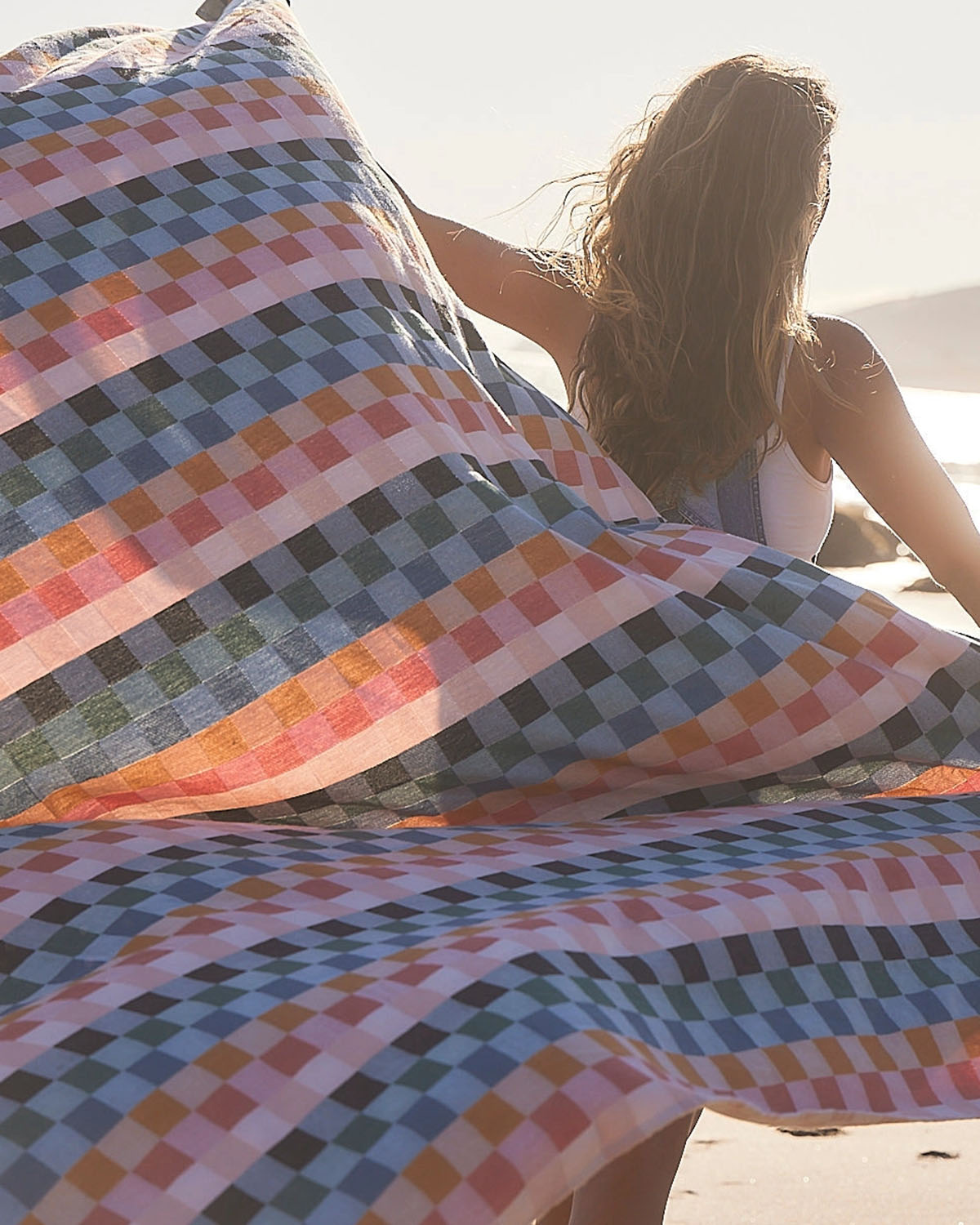 Colorful checkered blanket on a beach with a person sitting underneath