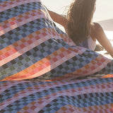 Colorful checkered blanket on a beach with a person sitting underneath