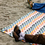 Person lying on a colorful geometric-patterned blanket on a sandy beach