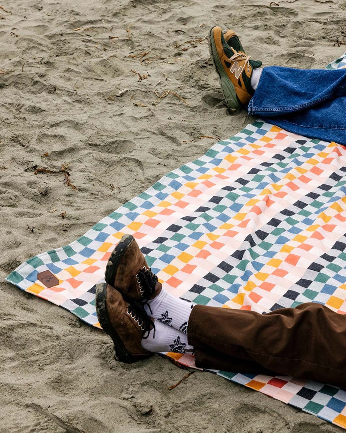 Person lying on a colorful geometric-patterned blanket on a sandy beach