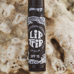 Lip balm stick with 'Lip Trip' branding on a textured beige background
